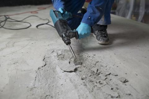 Arbeiter bearbeitet den Zementboden mit einem Presslufthammer, lizenzfreies Stockfoto