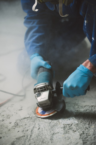 Arbeiter beim Glätten eines Zementbodens mit einem Winkelschleifer, lizenzfreies Stockfoto