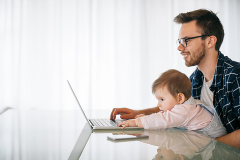 Junger Vater mit einem kleinen Mädchen auf dem Schoß am Laptop, lizenzfreies Stockfoto