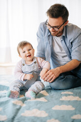 Porträt eines glücklichen kleinen Mädchens, das neben dem Vater auf einer Decke sitzt - BRF001301