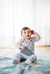 Portrait of baby girl sitting on blanket holding smartphone - BRF001302