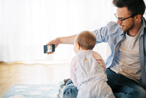 Vater sitzt auf einer Decke mit seiner kleinen Tochter und macht ein Selfie - BRF001306