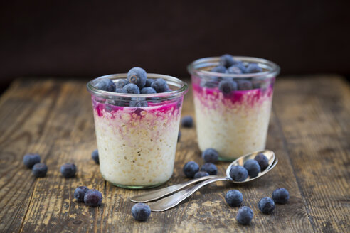 Zwei Gläser Overnight Oats mit Heidelbeeren und Beerensaft auf Holz - LVF004736