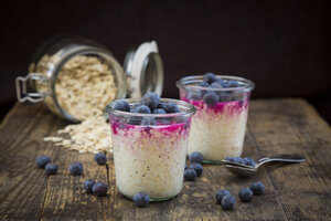 Zwei Gläser Overnight Oats mit Heidelbeeren und Beerensaft auf Holz - LVF004738