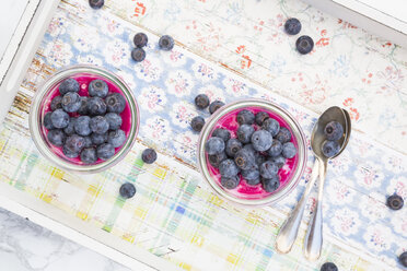 Two glasses of overnight oats with blueberries and berry juice on wooden tray - LVF004740