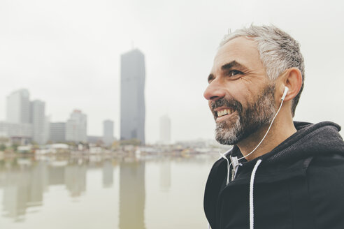 Austria, Vienna, portrait of smiling jogger with earphones in front of Donau City - AIF000319