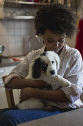 Junge Frau sitzt mit Hund auf dem Schoß in der Küche - MAUF000427