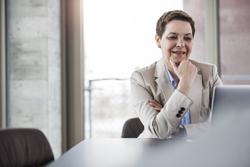 Lächelnde Geschäftsfrau am Schreibtisch mit Blick auf den Laptop - UUF006760