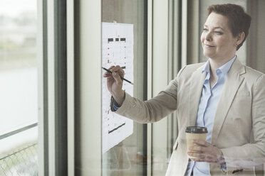 Confident businesswoman with construction plan at the window - UUF006767