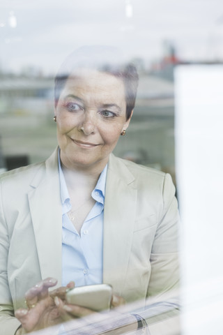 Geschäftsfrau mit Mobiltelefon hinter Fensterscheibe, lizenzfreies Stockfoto