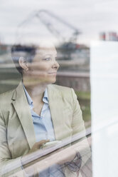 Businesswoman with cell phone behind windowpane - UUF006772
