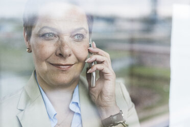 Businesswoman on cell phone behind windowpane - UUF006773