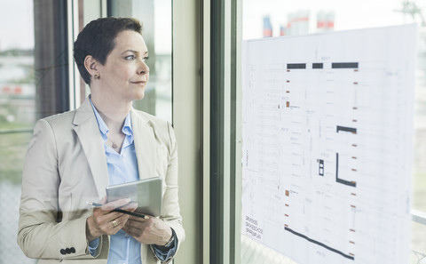 Geschäftsfrau am Fenster stehend mit Bauplan, lizenzfreies Stockfoto