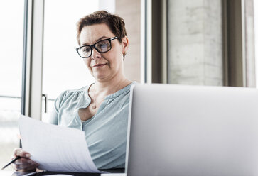 Geschäftsfrau beim Lesen von Dokumenten am Schreibtisch im Büro - UUF006785