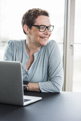 Smiling businesswoman with laptop in office - UUF006794