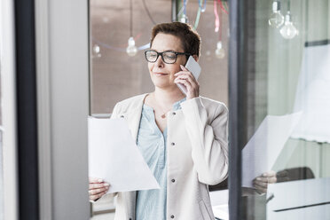 Businesswoman on cell phone reading document - UUF006807