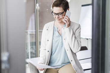 Businesswoman on cell phone reading document - UUF006808