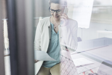 Geschäftsfrau am Mobiltelefon beim Lesen eines Dokuments - UUF006809