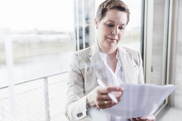 Businesswoman at the window reading document - UUF006810