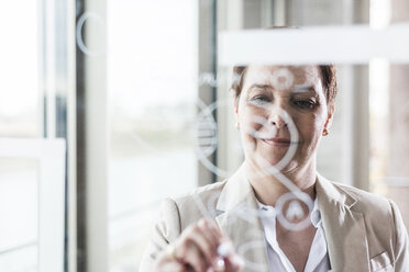 Businesswoman drawing on glass pane - UUF006812