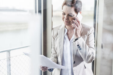 Businesswoman on cell phone reading document - UUF006813