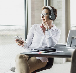Businesswoman with cell phone and headphones in office - UUF006821
