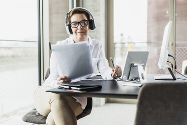 Geschäftsfrau mit Kopfhörern beim Lesen eines Dokuments im Büro - UUF006822