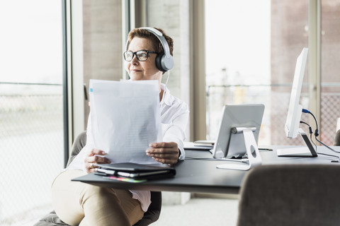 Geschäftsfrau mit Kopfhörer und Dokument im Büro, lizenzfreies Stockfoto