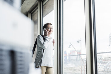 Frau am Handy schaut aus dem Fenster - UUF006838