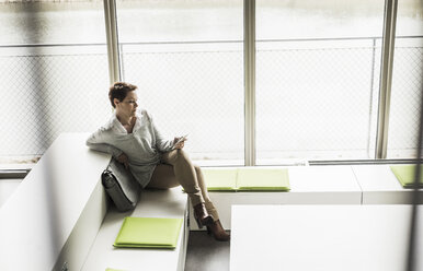 Woman with cell phone sitting in lobby - UUF006841