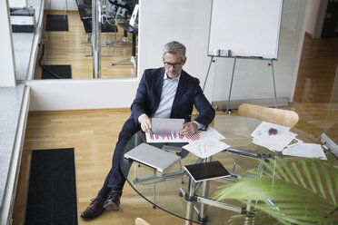 Successful businessman sitting in board room using digital tablet - RBF004268
