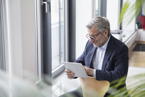 Erfolgreicher Geschäftsmann sitzt im Sitzungssaal und benutzt ein digitales Tablet - RBF004273