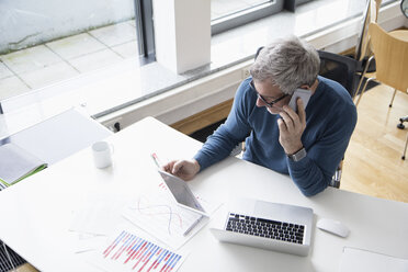 Mature man working in office with smart phone and digital tablet - RBF004275