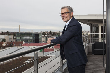 Successful businessman standing on office terrace looking over city - RBF004295