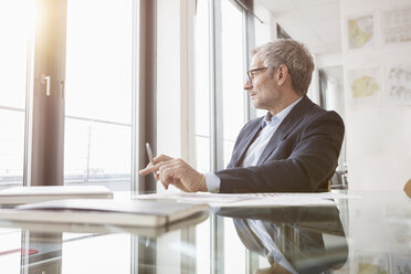 Successful businessman sitting at desk in his office - RBF004296