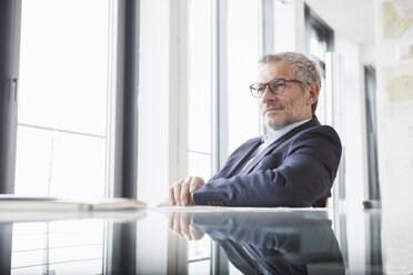 Erfolgreicher Geschäftsmann sitzt am Schreibtisch in seinem Büro - RBF004297