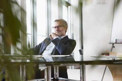 Erfolgreicher Geschäftsmann sitzt am Schreibtisch in seinem Büro, lizenzfreies Stockfoto