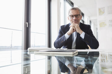 Erfolgreicher Geschäftsmann sitzt am Schreibtisch in seinem Büro - RBF004305