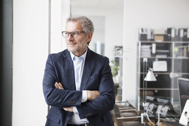 Successful businessman standing in his office with arms crossed - RBF004315