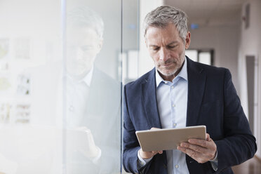 Erfolgreicher Geschäftsmann steht in seinem Büro und hält ein digitales Tablet - RBF004319