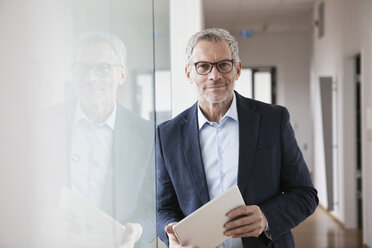 Successful businessman standing in his office holding digital tablet - RBF004320