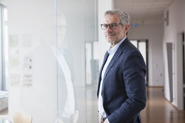 Successful businessman standing in his office looking out of window - RBF004322