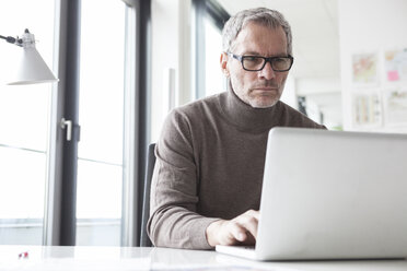 Älterer Mann sitzt im Büro und benutzt einen Laptop - RBF004333