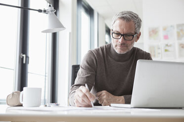 Älterer Mann sitzt im Büro und benutzt einen Laptop - RBF004334