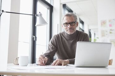 Älterer Mann sitzt im Büro und benutzt einen Laptop - RBF004335