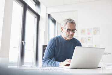 Mature man sitting in office using laptop - RBF004346