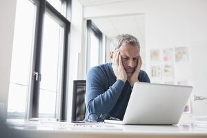 Älterer Mann sitzt im Büro und benutzt einen Laptop - RBF004349