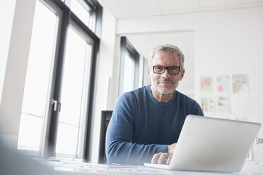 Älterer Mann sitzt im Büro und benutzt einen Laptop - RBF004350