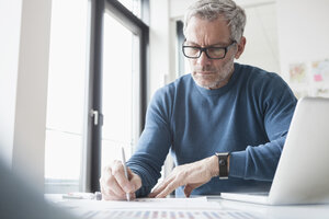 Älterer Mann sitzt im Büro und arbeitet mit Laptop und Smartwatch - RBF004352