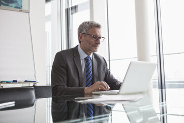 Älterer Manager sitzt im Büro und benutzt einen Laptop - RBF004354